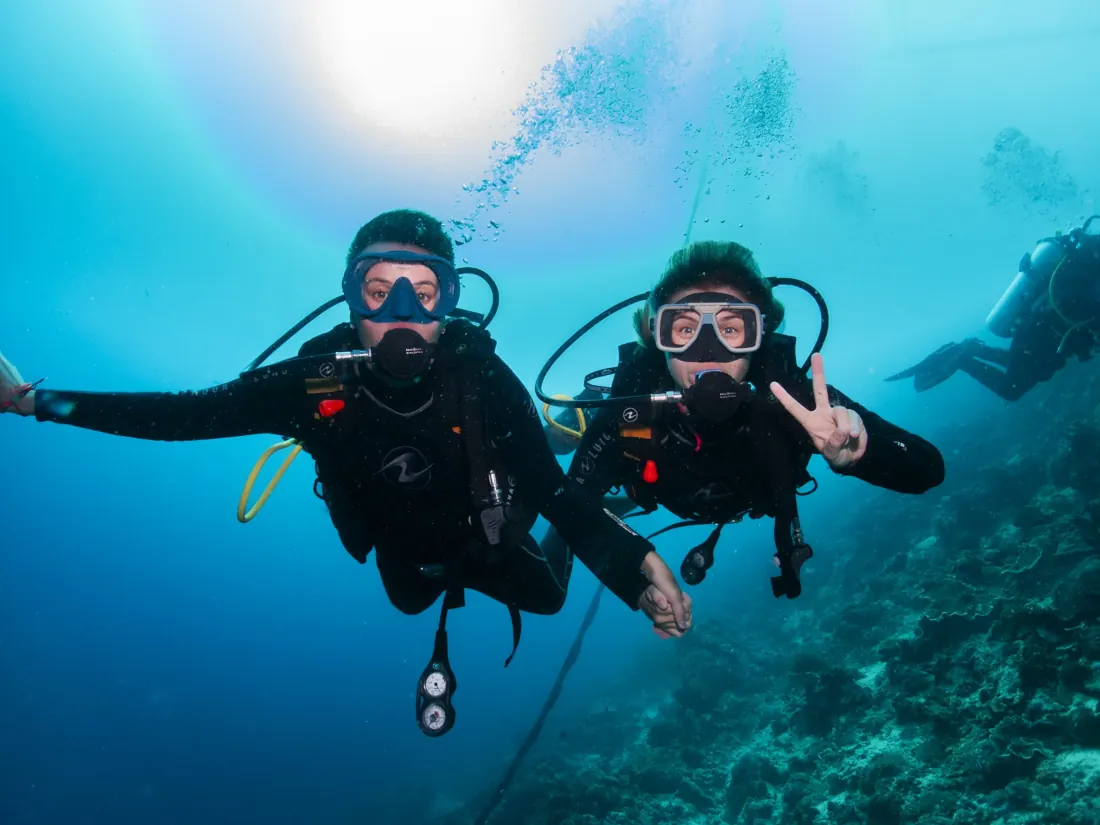 Two smiling divers in the blue, one making a peace sign